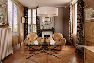 A room with a fireplace, leather armchairs, a glass coffee table, and a large chandelier.