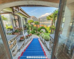Escadaria de pedra leva a uma varanda com carpete azul, cercada por plantas em vasos e vista para montanhas.