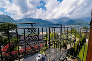 Uma varanda com cadeira e mesa de metal, com vista para uma paisagem montanhosa e um corpo d'água.