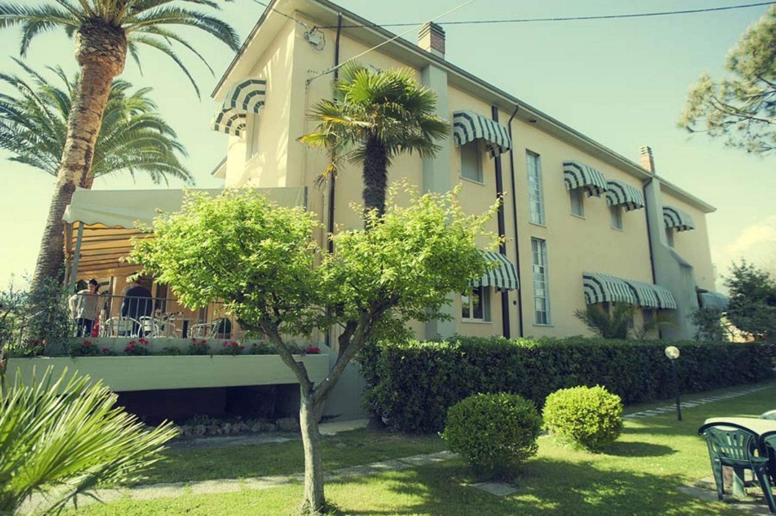 A two-story building with a flat roof, a balcony, and a well-maintained garden with various plants and a tree.