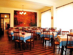 A dining area with multiple tables and chairs, a large painting on the wall, and a staircase leading to another level. - Hotel Parma Mare (Massa)