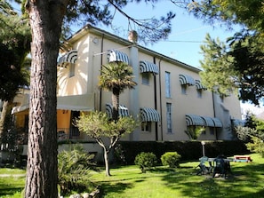 A multi-story building with a symmetrical facade, striped awnings over windows, and a well-maintained lawn with a picnic table. - Hotel Parma Mare (Massa)