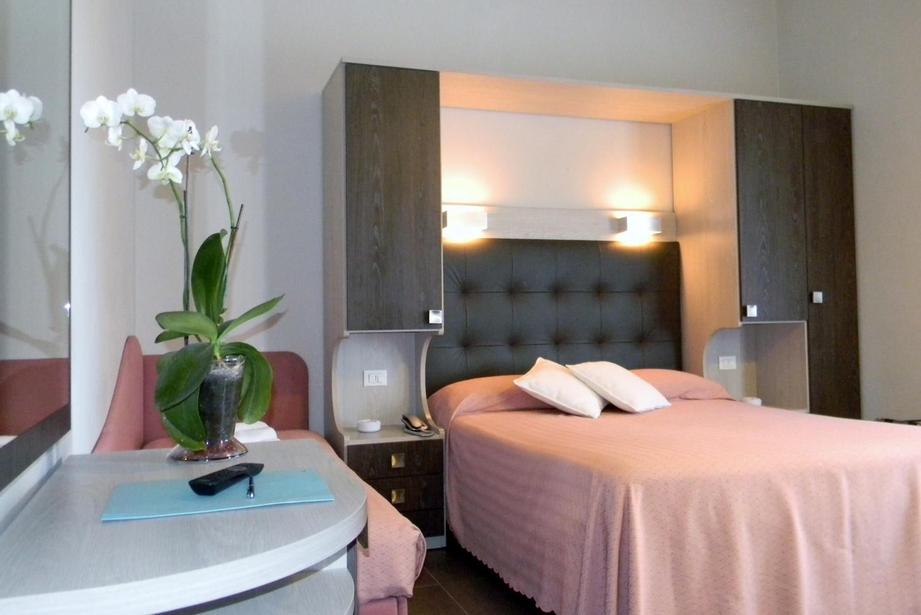 Une chambre d’hôtel comprenant un lit, des tables de chevet, un bureau avec une chaise et une plante en pot.