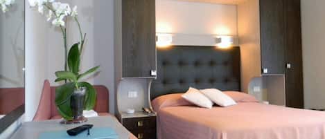 Una habitación de hotel con una cama, mesitas de noche, un escritorio con una silla y una planta en maceta.