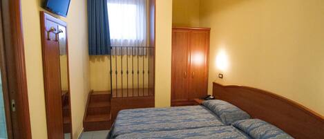 Une chambre d’hôtel avec un lit, une armoire, une télévision et une fenêtre avec des rideaux.