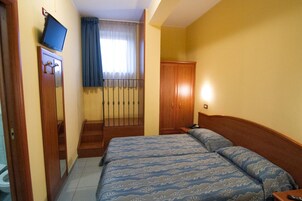 A hotel room with a bed, a wardrobe, a television, and a window with curtains.