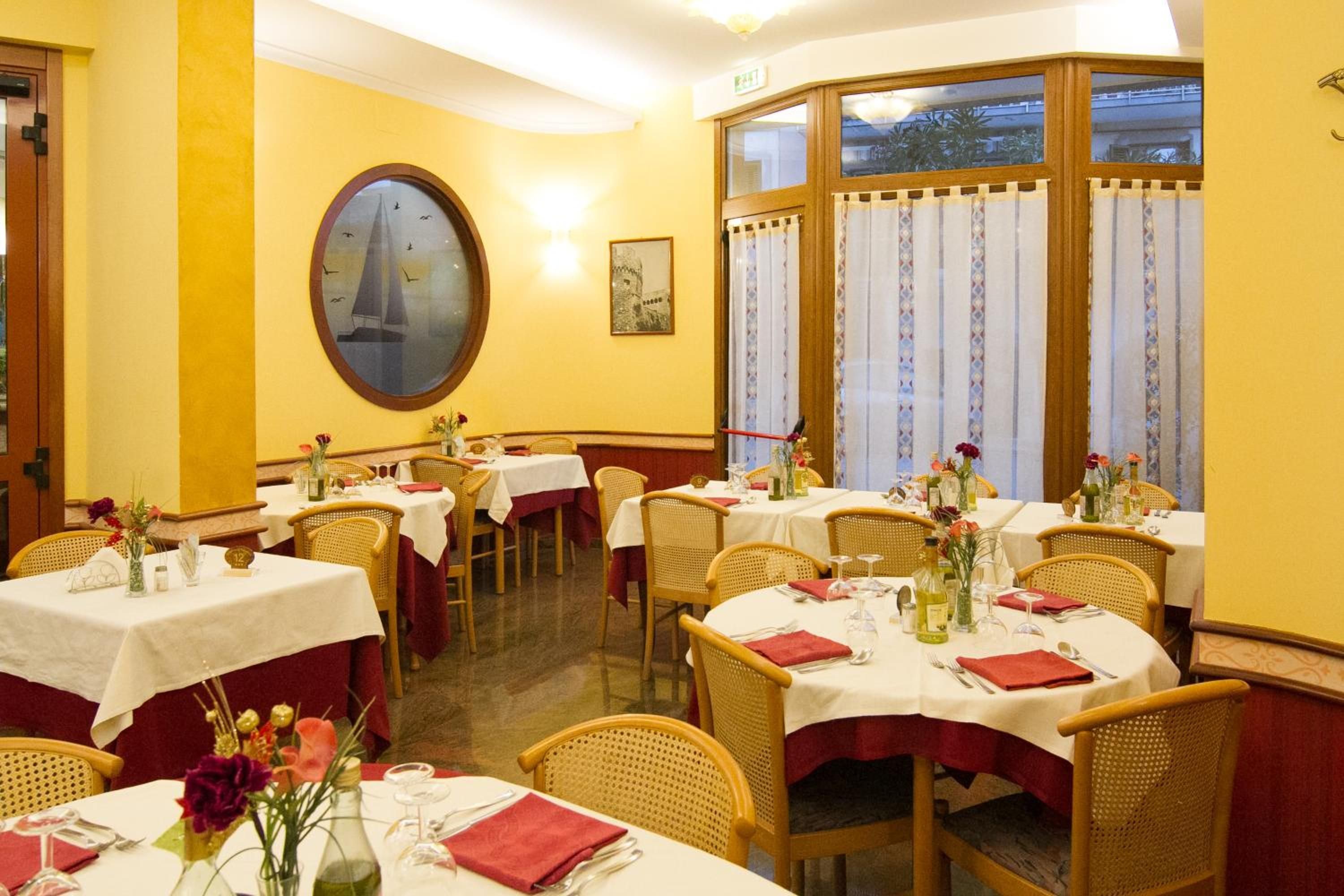 Un'area pranzo con tavoli rotondi, sedie in vimini e pareti gialle.
