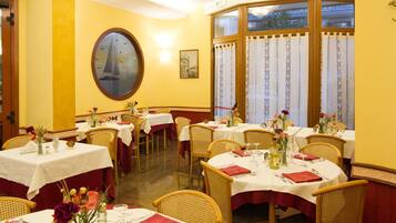 Un'area pranzo con tavoli rotondi, sedie in vimini e pareti gialle.