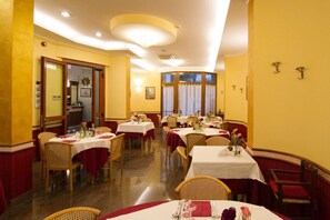 Un restaurante con varias mesas y sillas, un reloj en la pared y una puerta que conduce a otra habitación.