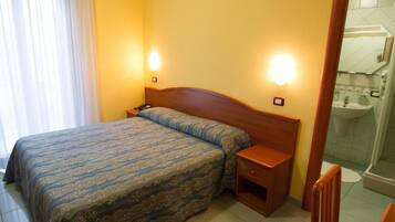 Una camera d'albergo con un letto, comodini, uno specchio e un bagno con lavandino e specchio.