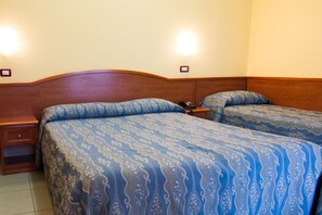 Habitación de hotel con dos camas, cada una con cabecera y mesita de noche.