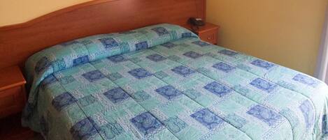 Habitación estándar de hotel con una cama individual, cabecera de madera, mesita de noche con teléfono y una lámpara de pared.