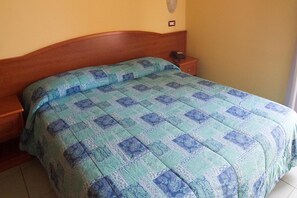 Habitación estándar de hotel con una cama individual, cabecera de madera, mesita de noche con teléfono y una lámpara de pared.