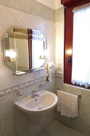 Un baño con un espejo grande, un lavamanos, un perchero para toallas y una ventana con cortinas.