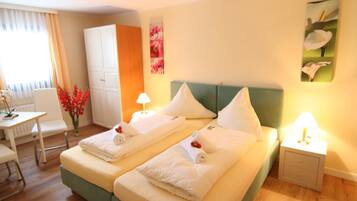 A hotel room with a bed, two bedside tables with lamps, a desk, a chair, a wardrobe, and a vase with flowers.