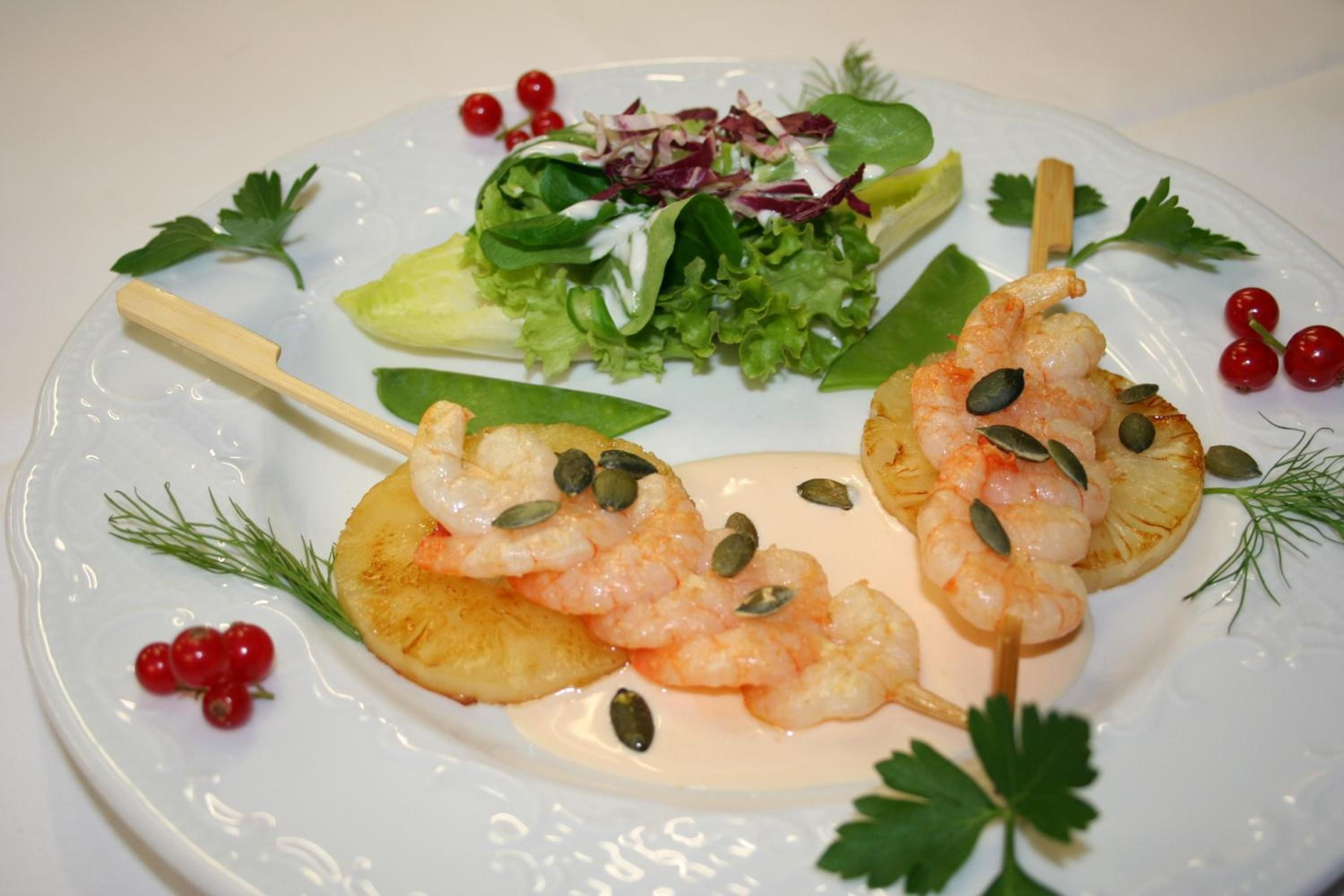 Ein Teller mit Garnelen-Spießen, Salat und Dekoration.