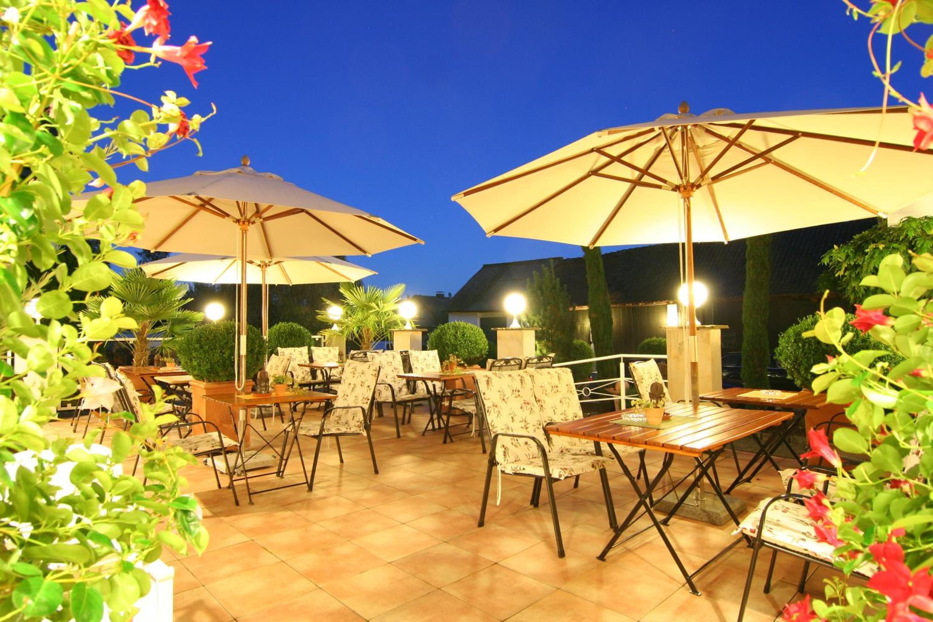 Un espace extérieur aménagé en terrasse, avec des tables et des chaises, de grands parasols et des plantes en pot.