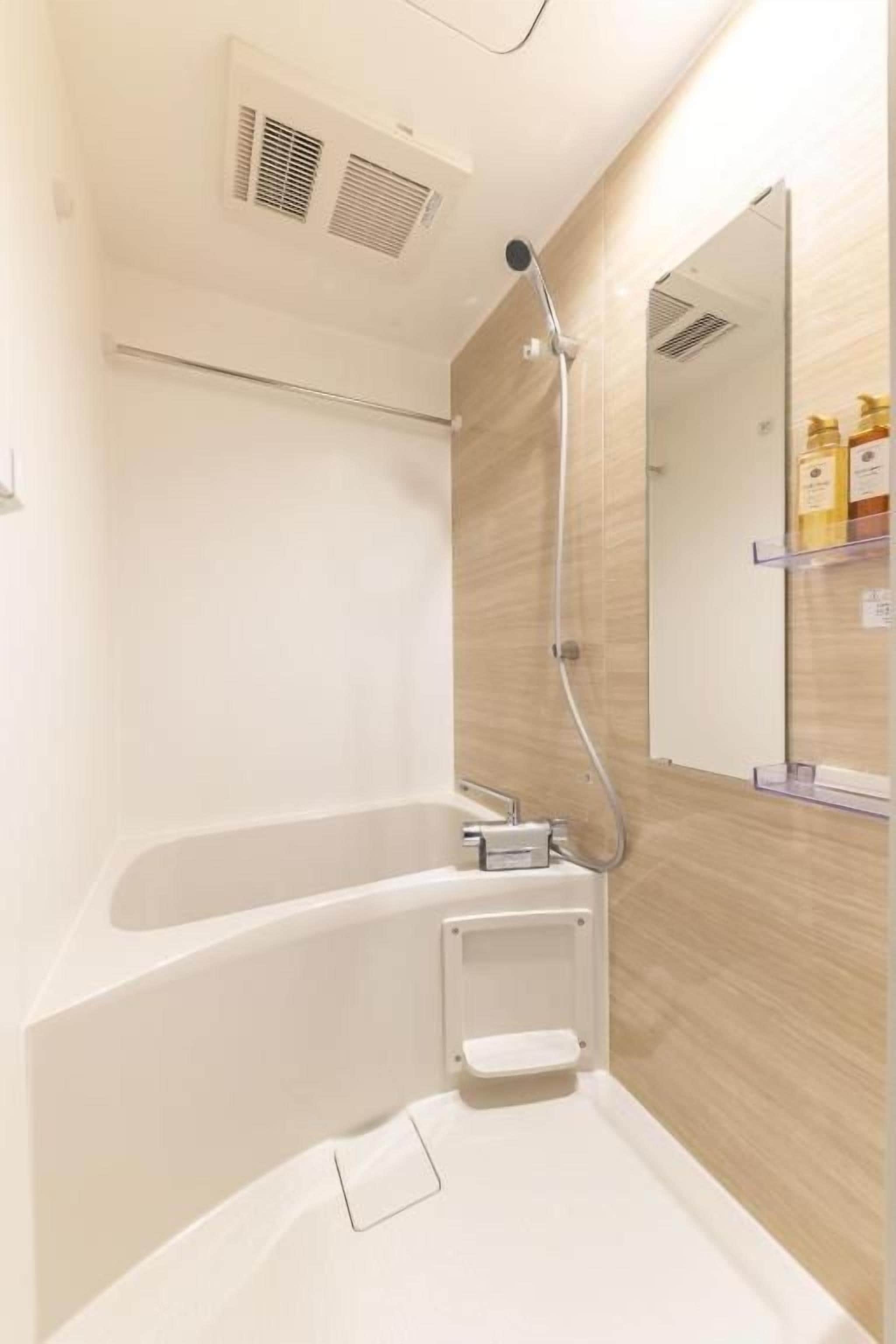 Et badeværelse med badekar, brusebad, spejl og et hylder med toiletartikler.