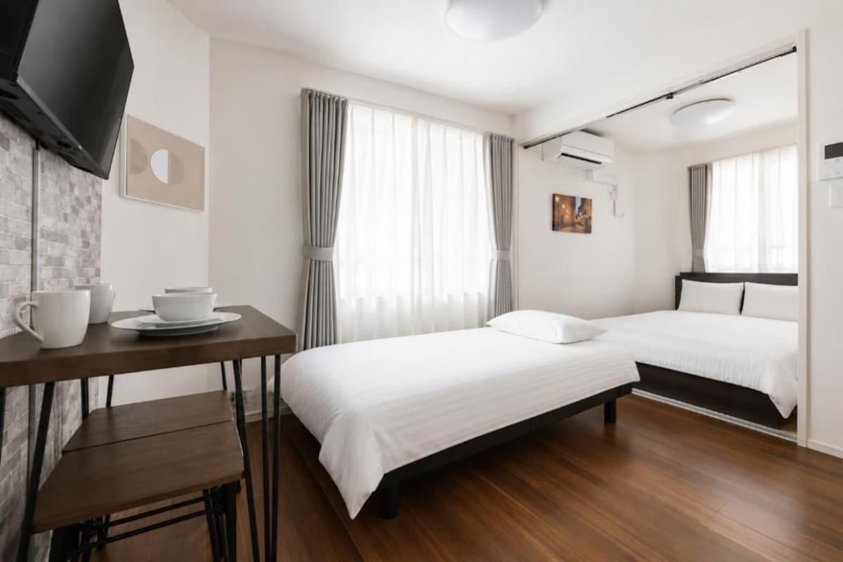 Ein Hotelzimmer mit Bett, Nachttischen, einem Flachbildfernseher und einem fensterbelaubten Fenster.