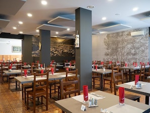 Un restaurant doté de nombreuses tables et chaises, d’un sol à motifs et d’une grande fresque murale.