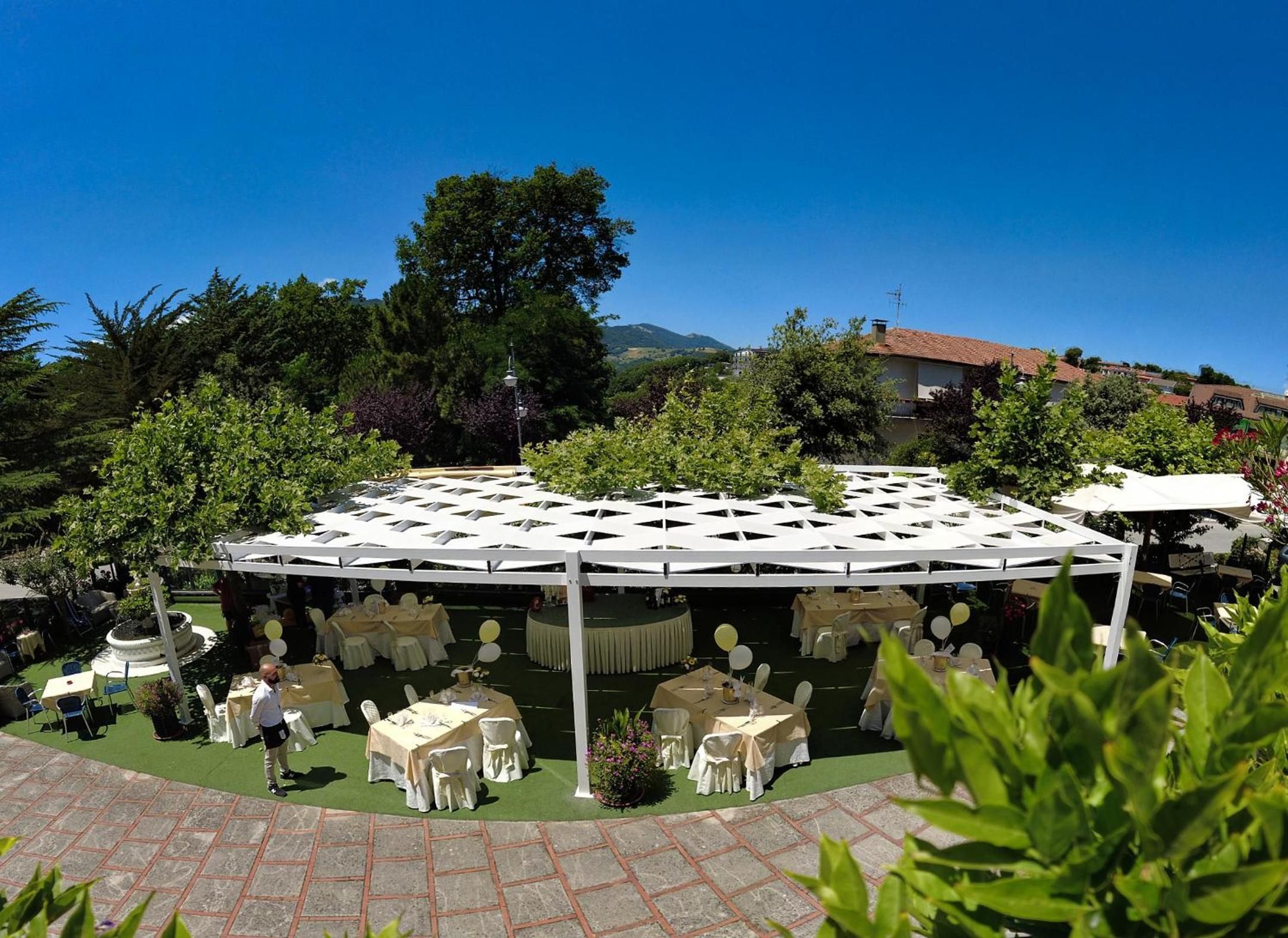 Un espacio para eventos al aire libre con mesas redondas y toldos blancos, rodeado de follaje y un cielo despejado.
