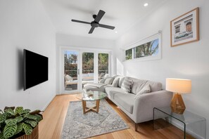 A modern living room with a sofa, a glass coffee table, a TV, a ceiling fan, and a lamp.