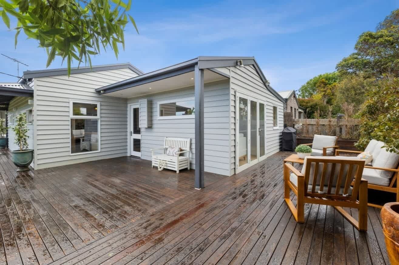 A covered patio with a wooden deck, a white bench, and a table with chairs.