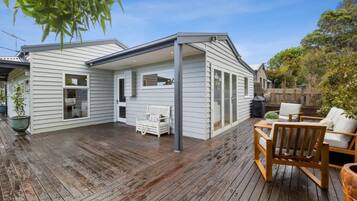 A covered patio with a wooden deck, a white bench, and a table with chairs.
