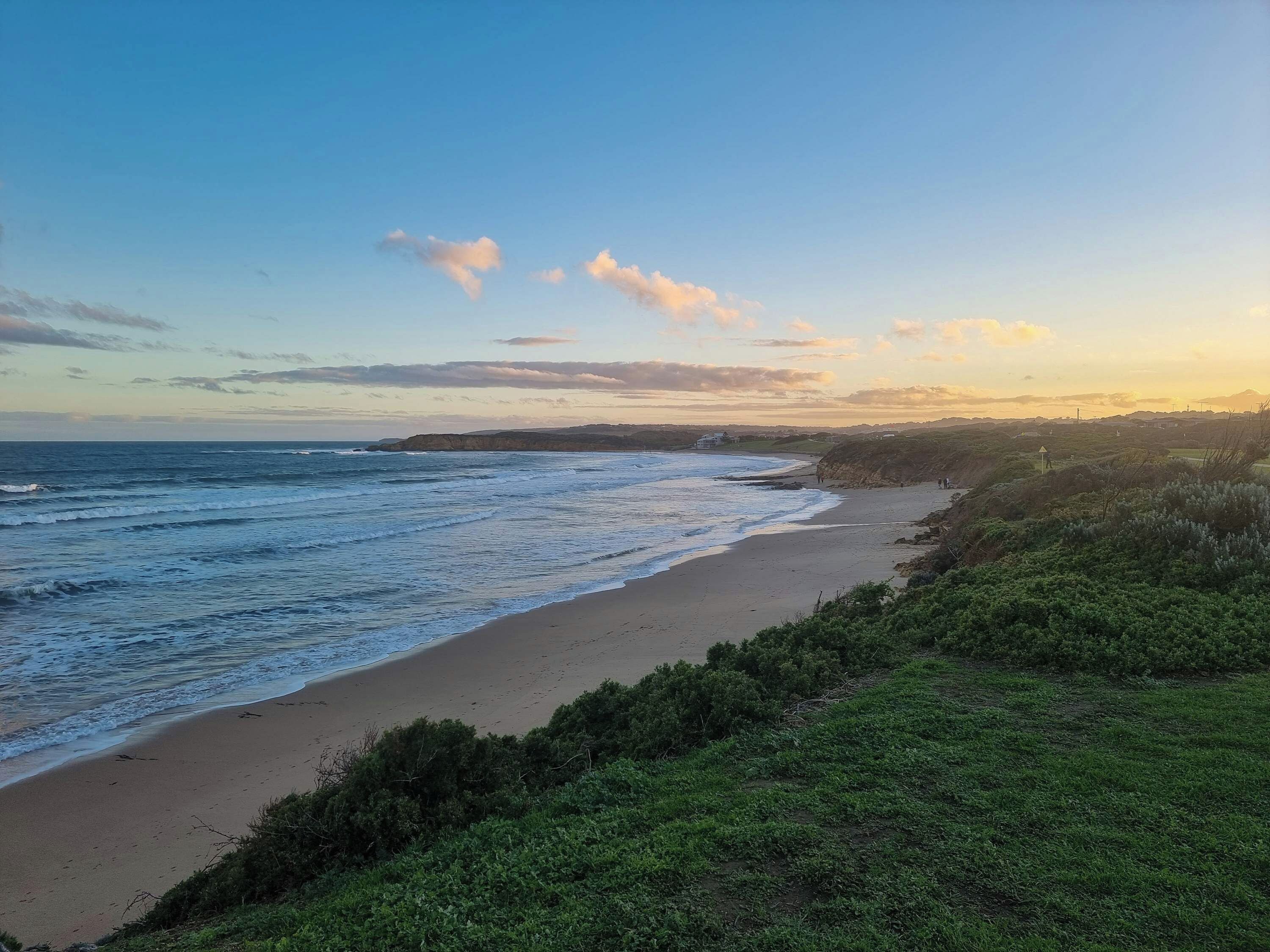 A coastal landscape with a beach, grassy areas, and a distant shoreline.