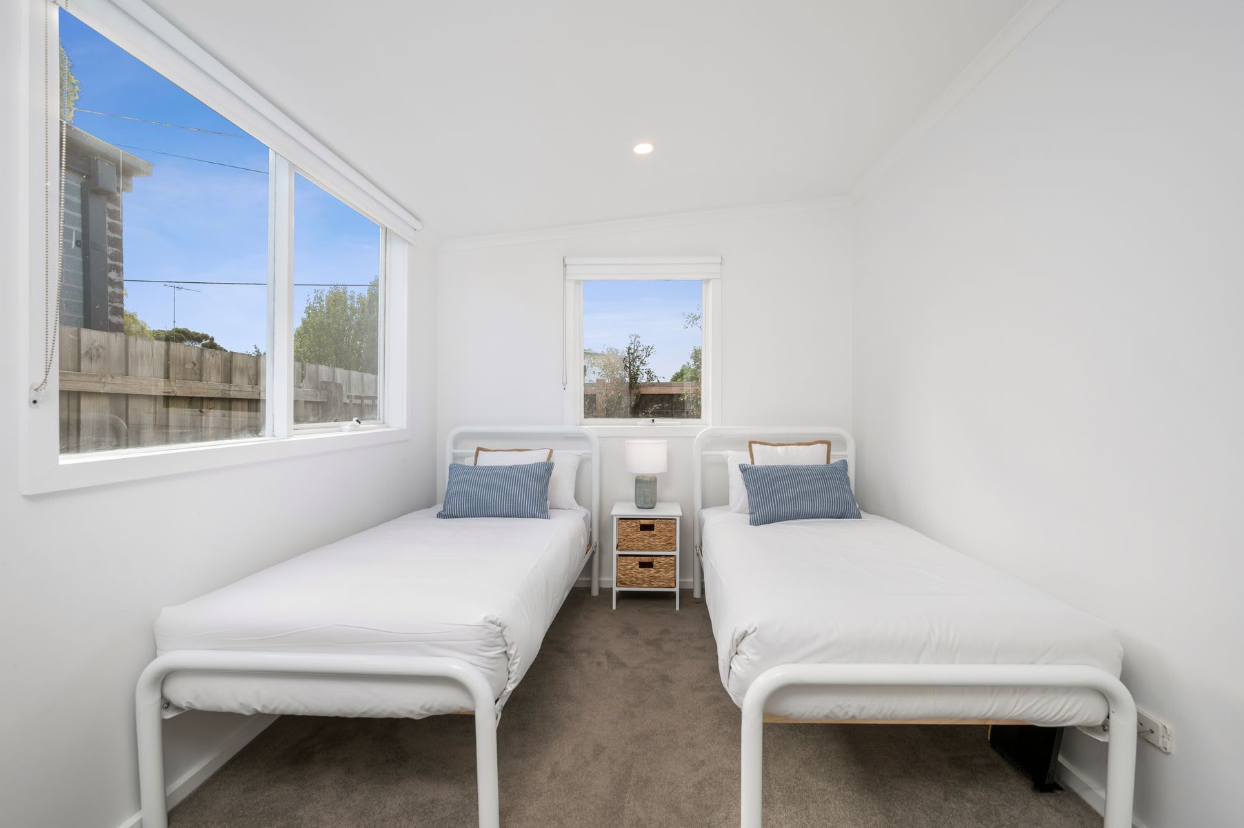 Une petite chambre propre, avec deux lits simples, une fenêtre et un miroir.
