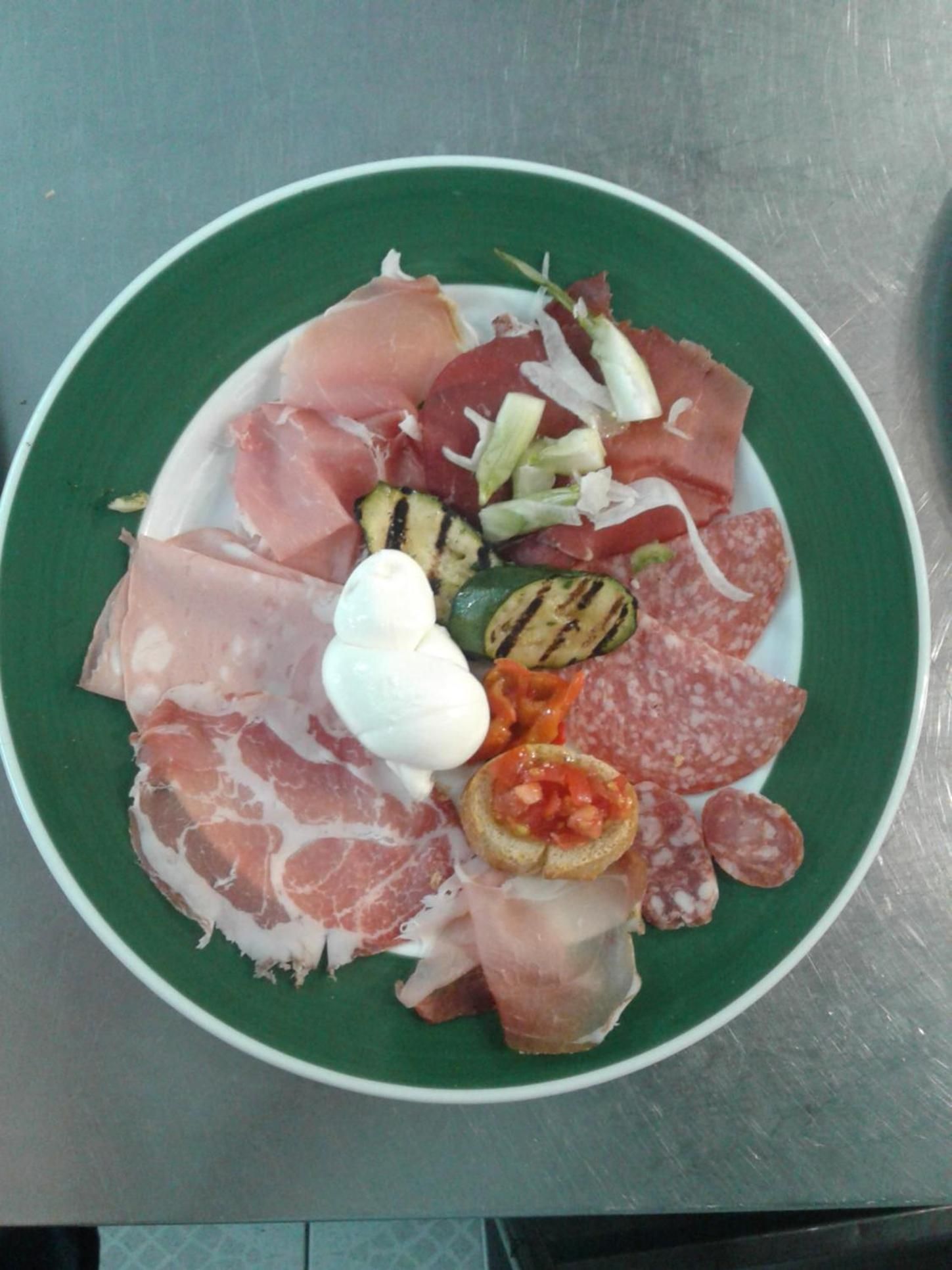 A plate of assorted meats and vegetables, including prosciutto, salami, and grilled zucchini.