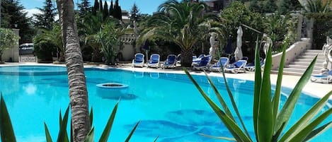 Una piscina azul cristalina con sillas de descanso y palmeras.