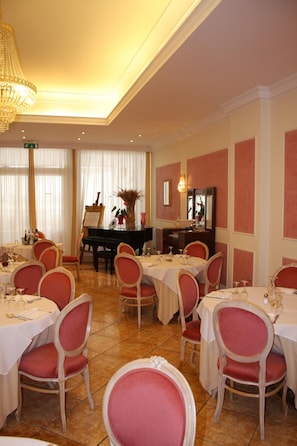 A dining area with tables set for service, chairs, a piano, and a chandelier. - Grand Hotel Degli Angeli (San Giovanni Rotondo)