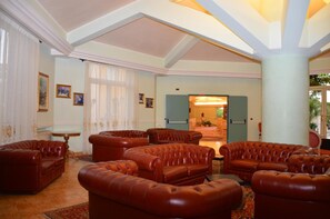 A spacious living room with leather sofas, a dining area, and a view of the kitchen through an open door. - Grand Hotel Degli Angeli (San Giovanni Rotondo)