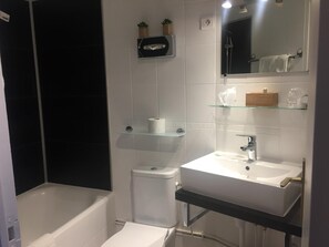 A modern bathroom with a bathtub, toilet, and sink. There are shelves with toiletries and a mirror above the sink.