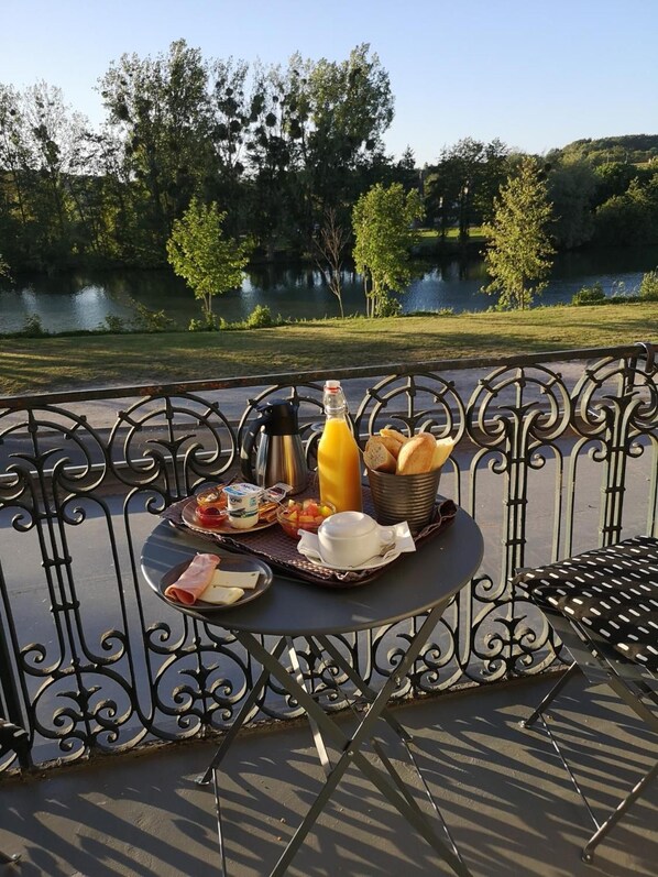 A table set outdoors with a view of a lake and trees, featuring breakfast items like bread, cheese, and juice.