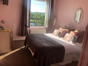 A bedroom with a bed, a desk, a chair, a window with a view, and a radiator.