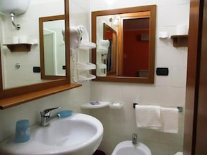 Casa de banho com lavatório, espelho, sanita e secador de cabelo numa prateleira.