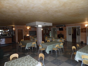 Uma área de refeições com mesas e cadeiras, um bar com garrafas e uma televisão.