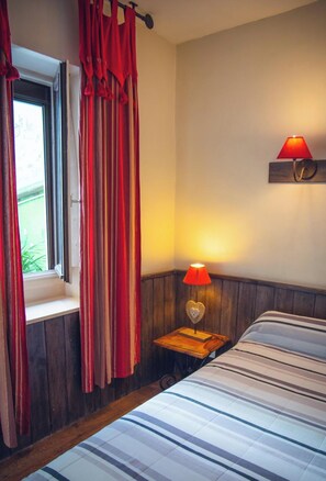 Quarto com cama, janela com cortinas, abajur e luminária na parede.
