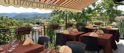 Un área de comedor al aire libre con mesas dispuestas para dos, con vistas a un paisaje pintoresco.