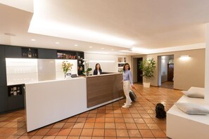 Een hotel receptie met een receptiebalie, een zithoek en een potplant.