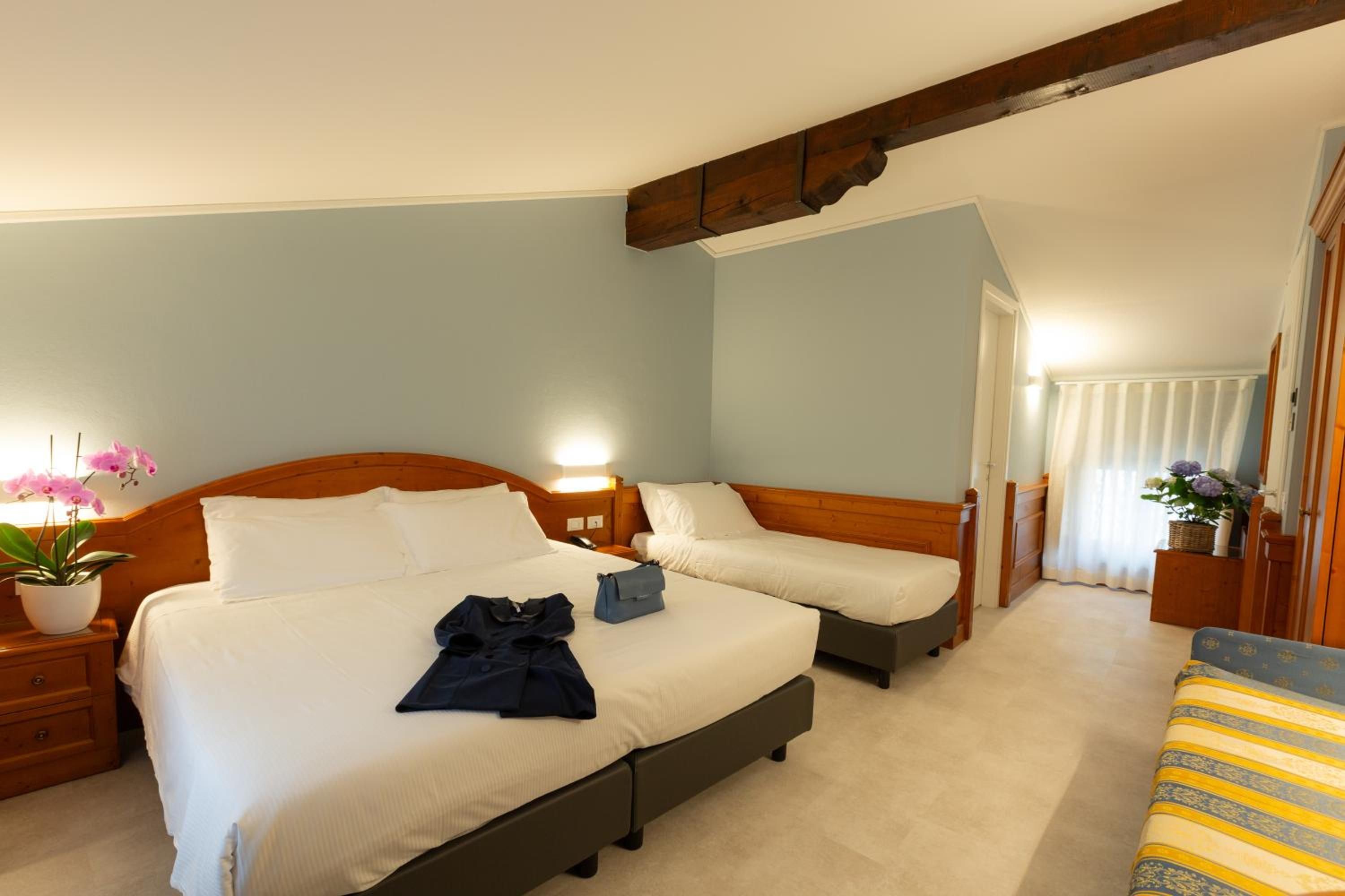 A hotel room with two beds, a wooden headboard, a nightstand, a potted plant, and a view of the corridor.