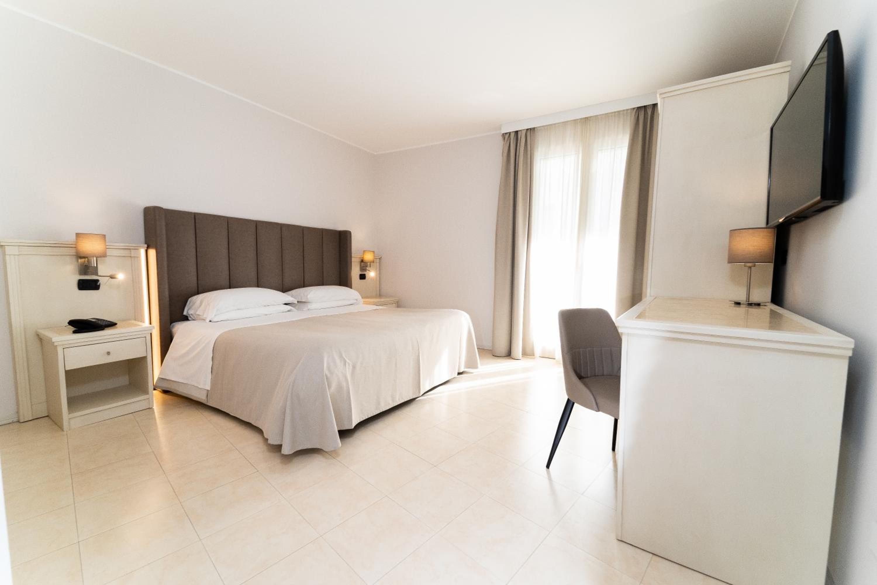 Una habitación de hotel con una cama, mesitas de noche, un escritorio, una silla y un televisor.