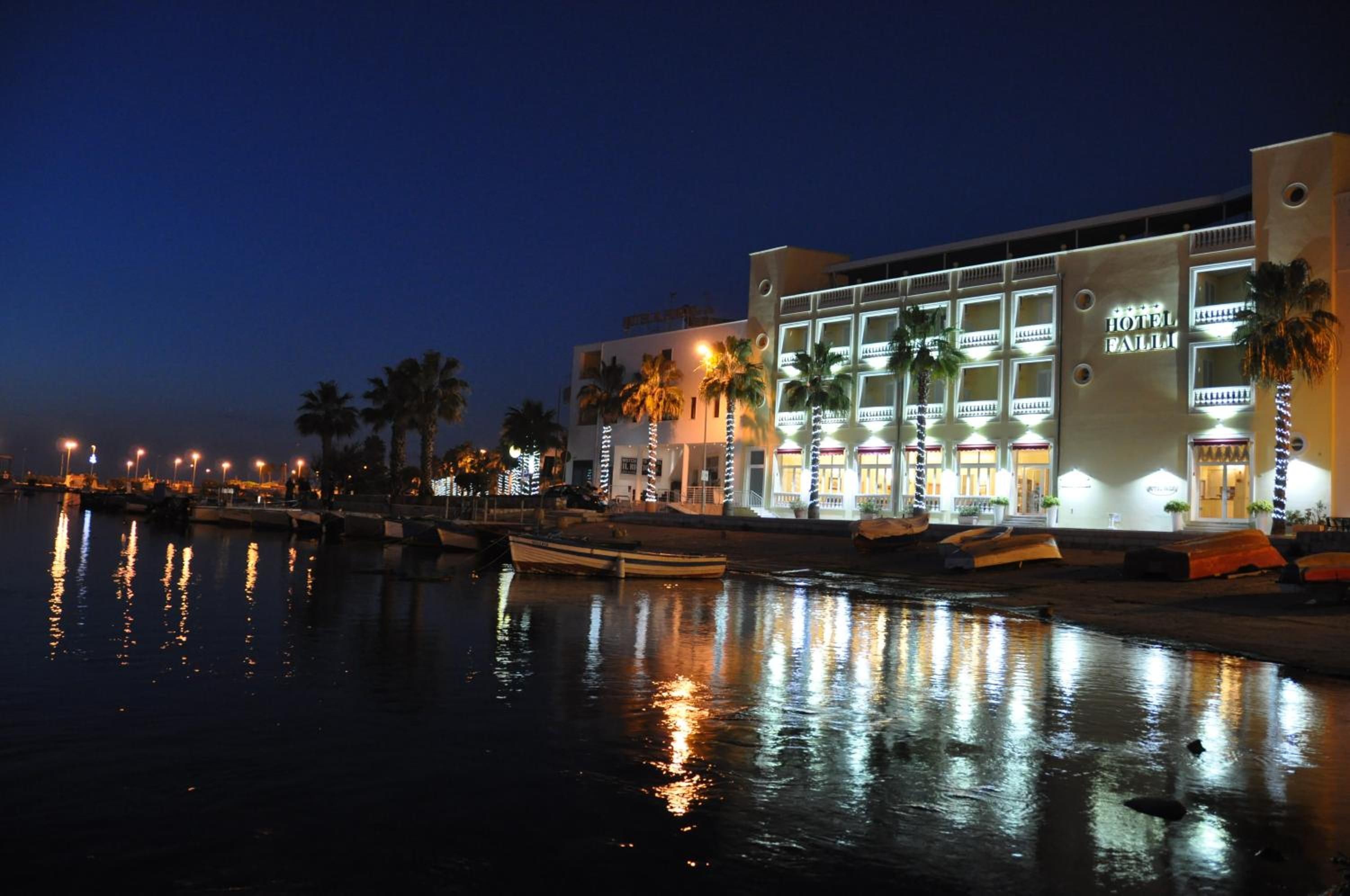 A hotel with a modern facade, a waterfront view, and a reflection of the building in the water.