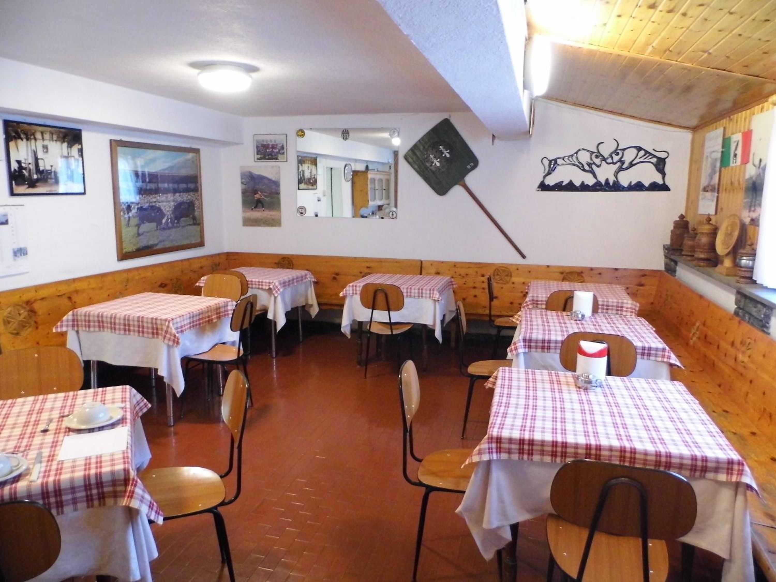 A restaurant interior with tables set for dining, wooden paneling on the walls, and artwork on the walls.
