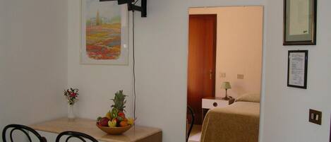A small room with a bed, a desk with a chair, a television, and a framed picture on the wall.