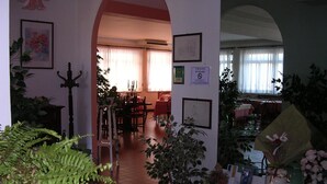 Un interior que inclou una zona de menjador, un saló i una cuina. Hi ha plantes en testos i quadres a les parets.