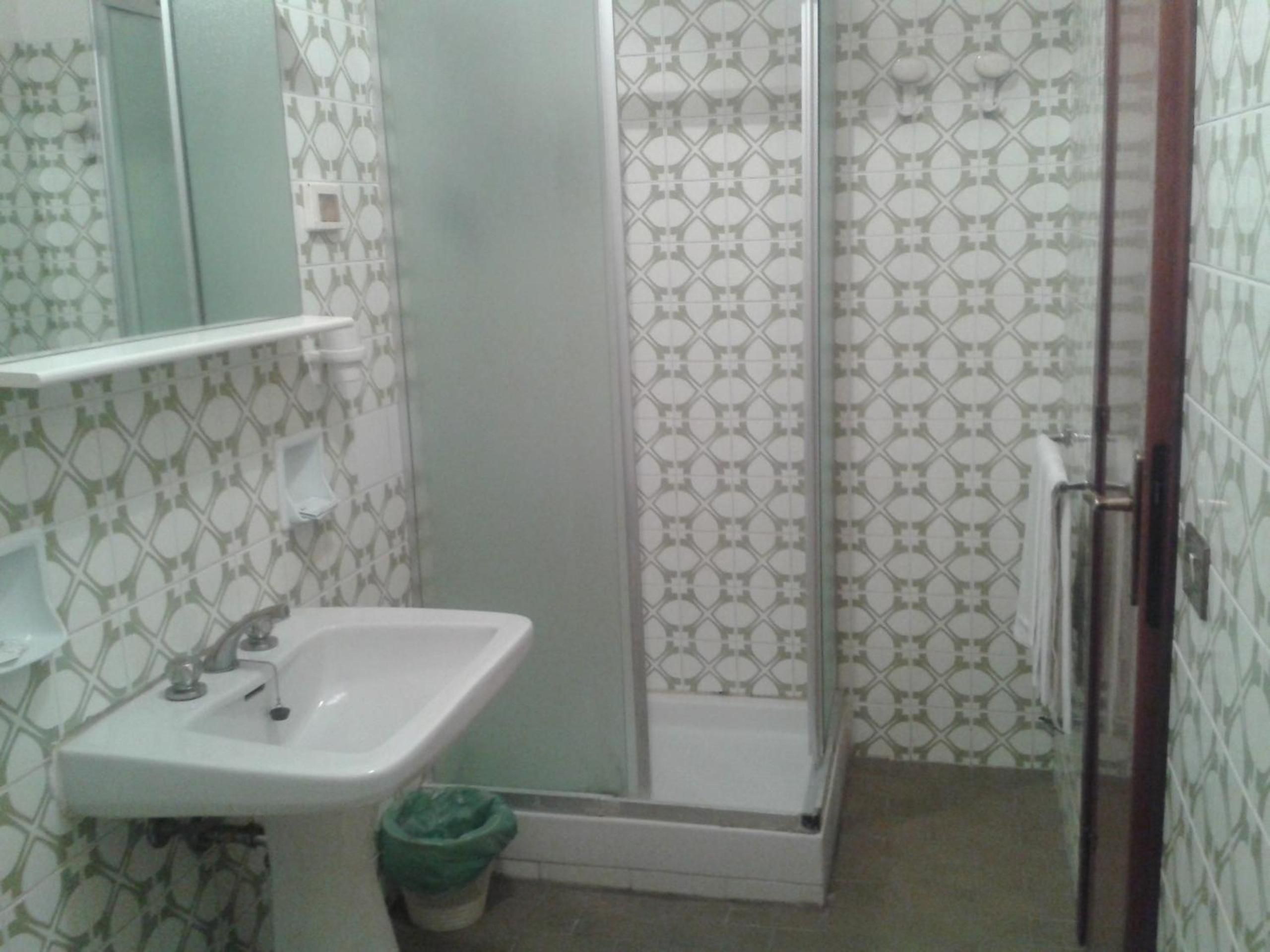 Un bagno con un lavandino bianco, uno specchio e un box doccia con piastrelle decorate.