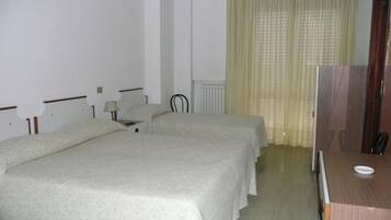 Una camera d'albergo con due letti, una scrivania, una sedia, un termosifone e una televisione.